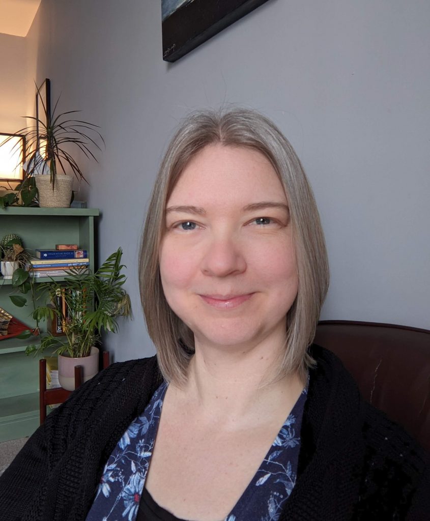 Photograph of Linzi with green bookshelf and lamp in the background.